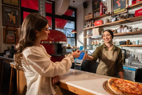 Gast betaalt contactloos met haar telefoon op een myPOS Ultra pinapparaat aan de bar van een pizzeria